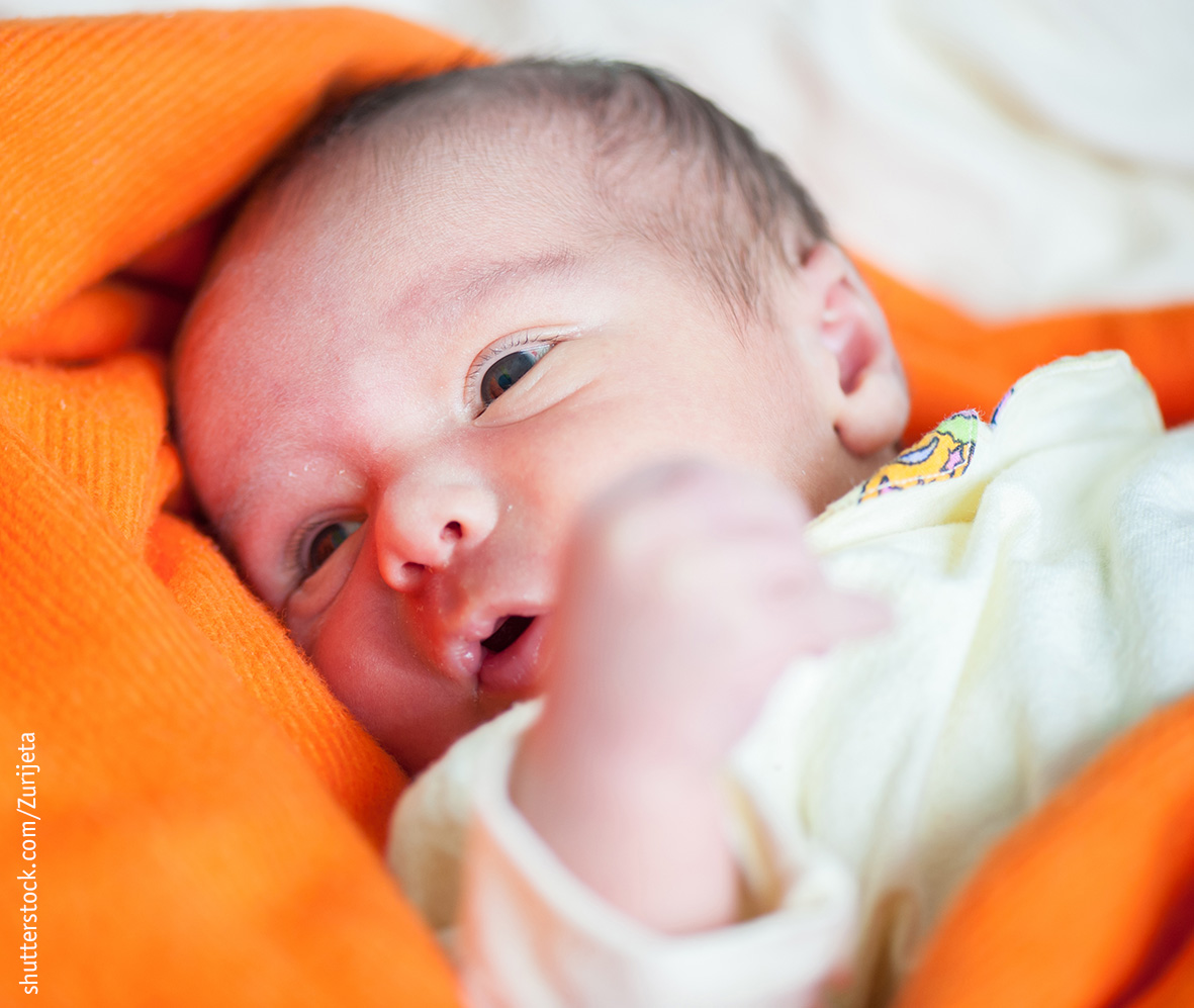 Neugeborenes mit offenen Augen, das auf einer orangen Decke liegt